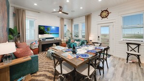 A spacious living room with a large flat-screen TV, a dining area with a wooden table set for four, and a cozy seating area with a fireplace.