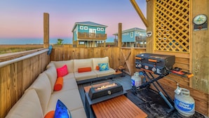 A wooden deck with a sofa, a grill, and a propane tank.