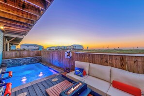 A pool area with a wooden deck, a fire feature, and a sofa with cushions. - Private Pool~Walk to Beach~Pets! (Port Aransas)