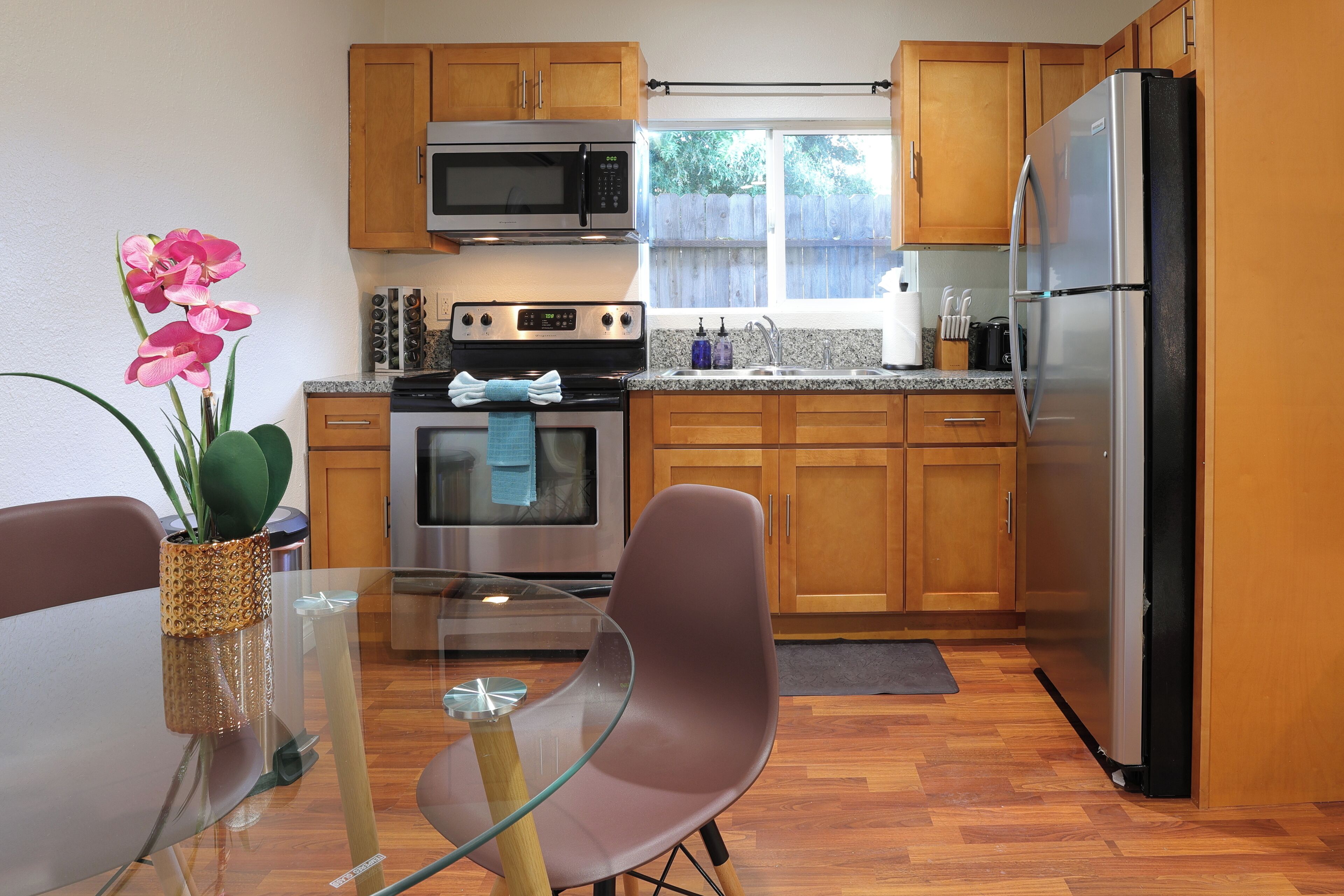 A modern kitchen with wooden cabinets, stainless steel appliances, and a glass dining table with chairs.