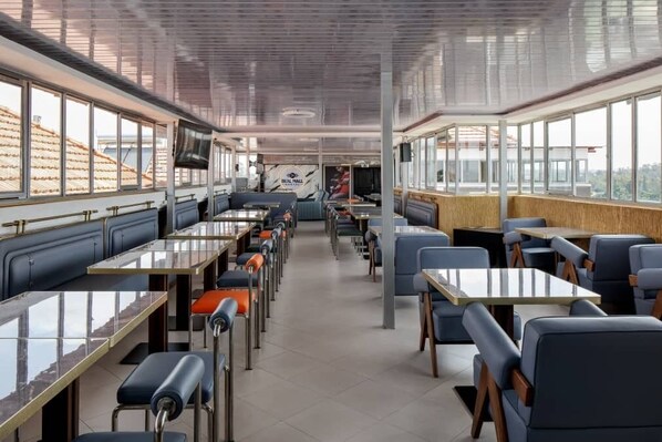 Un restaurante con mesas altas, cabinas, amplias ventanas y una decoración interior moderna.
