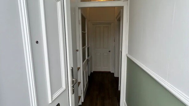 A narrow hallway with a white door on the left, a wooden floor, and a green wall. - Welcome to The Pink House managed by Sean! (Torquay)
