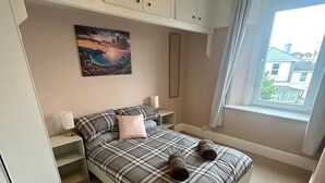 A bedroom with a bed, bedside tables, a painting, a window, and a hanging light fixture. - Welcome to The Pink House managed by Sean! (Torquay)