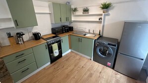 A compact kitchen with green cabinets, a wooden countertop, a built-in oven, a washing machine, and a refrigerator. - Welcome to The Pink House managed by Sean! (Torquay)