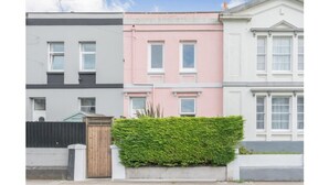 A row of three townhouses with distinct pastel colors, a wooden gate, and a neatly trimmed hedge in the foreground. - Welcome to The Pink House managed by Sean! (Torquay)