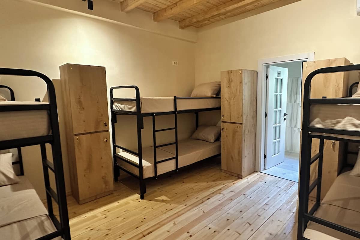 A room with bunk beds, wooden flooring, and a door leading to another room.