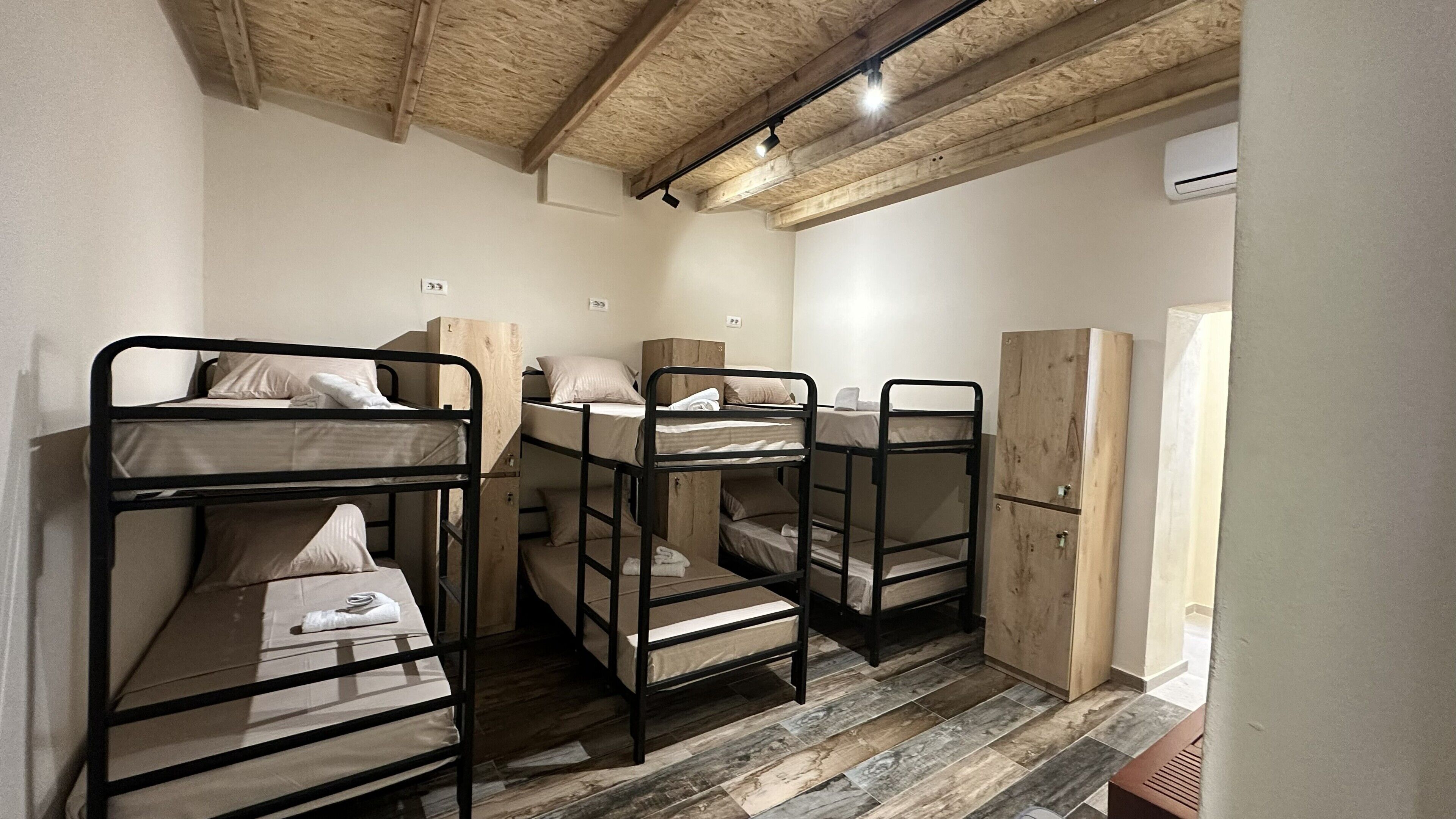 Des lits superposés avec des structures en bois, une armoire et un appareil de climatisation dans une pièce dont le plafond est également en bois.