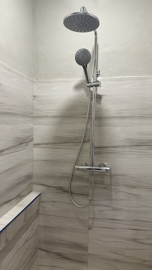 Une douche équipée d’un pommeau de douche à main et d’un pommeau fixé au mur, le tout installé devant un mur carrelé dont le motif rappelle le marbre.