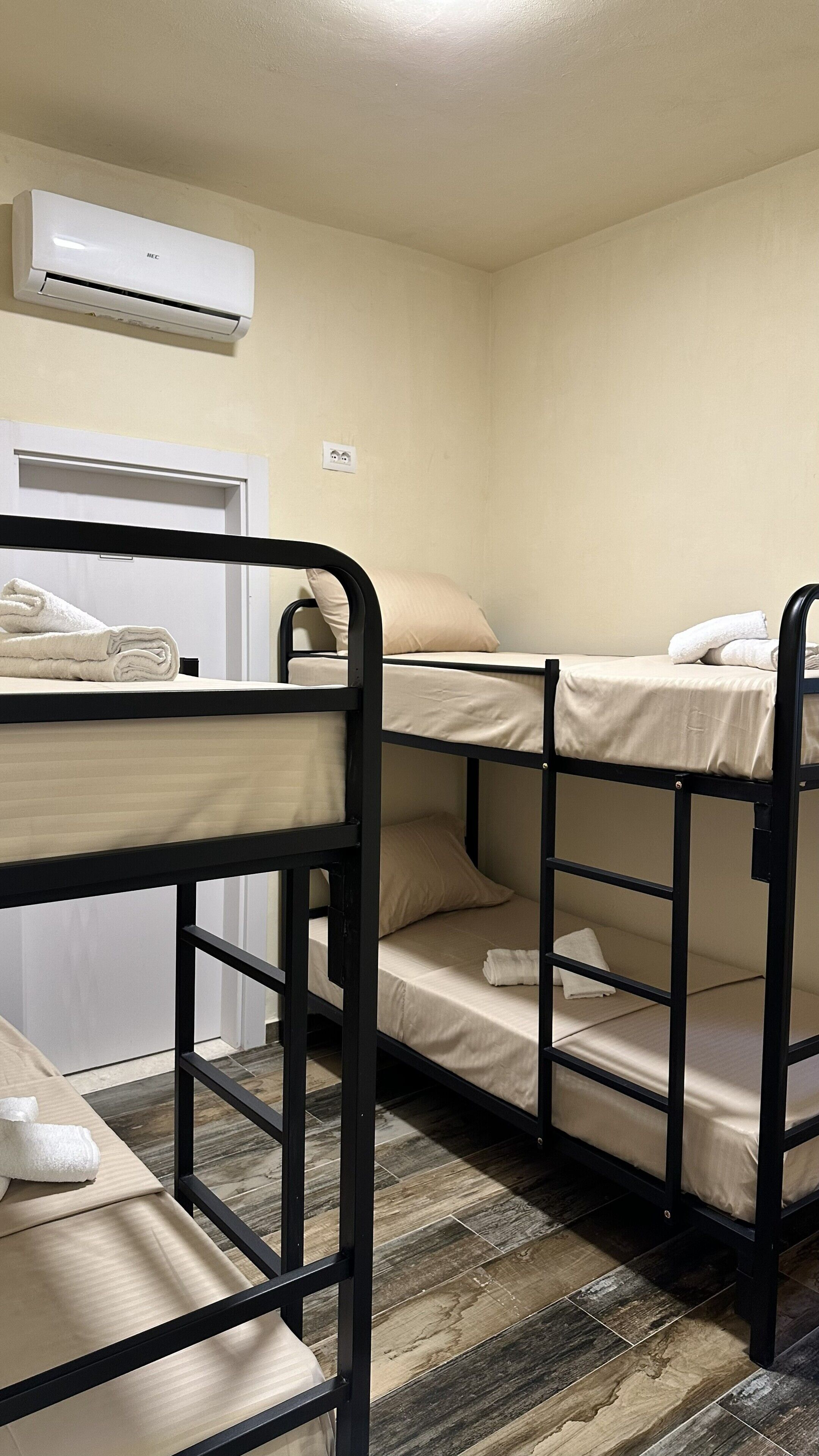 Une chambre avec un lit superposé, un climatiseur blanc, une porte et un sol carrelé.