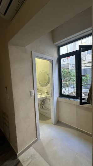 A room with a bathroom, a window with a view of the outside, and a door leading to another room.