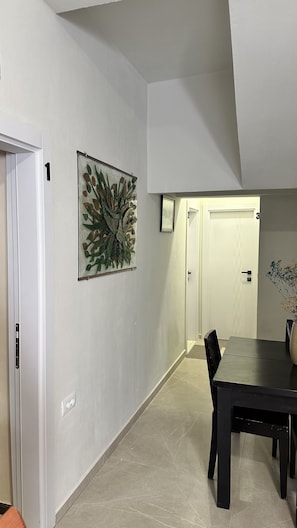 A hallway with a dining table, chairs, a door, and a wall-mounted artwork.