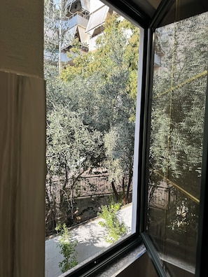 A window view of a courtyard with trees and a brick wall.
