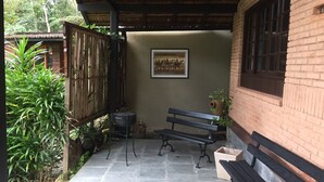 Ein überdachter Patio-Bereich mit einer Bank, einem kleinen Tisch und einem Grill.