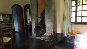 Ein Zimmer mit Kamin, einem Holzstuhl, einem Bett mit Decke und einem Fenster mit Vorhängen.