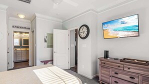 Una camera da letto con un letto, una cassettiera, una sveglia e una TV che mostra una spiaggia.