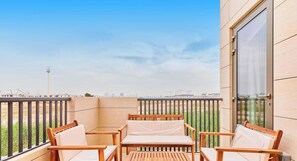 Un balcon avec une table et des chaises en bois, une vue sur le paysage urbain et une grande fenêtre.