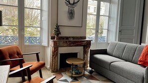 Un accogliente soggiorno con camino, divano e poltrona. Una grande finestra offre vista su alberi e include un balcone.