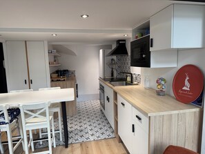 A modern kitchen with white cabinetry, a wooden countertop, and a dining area with white chairs. - Le Balcon d'Etigny - T2 apartment (Bagnères-de-Luchon)