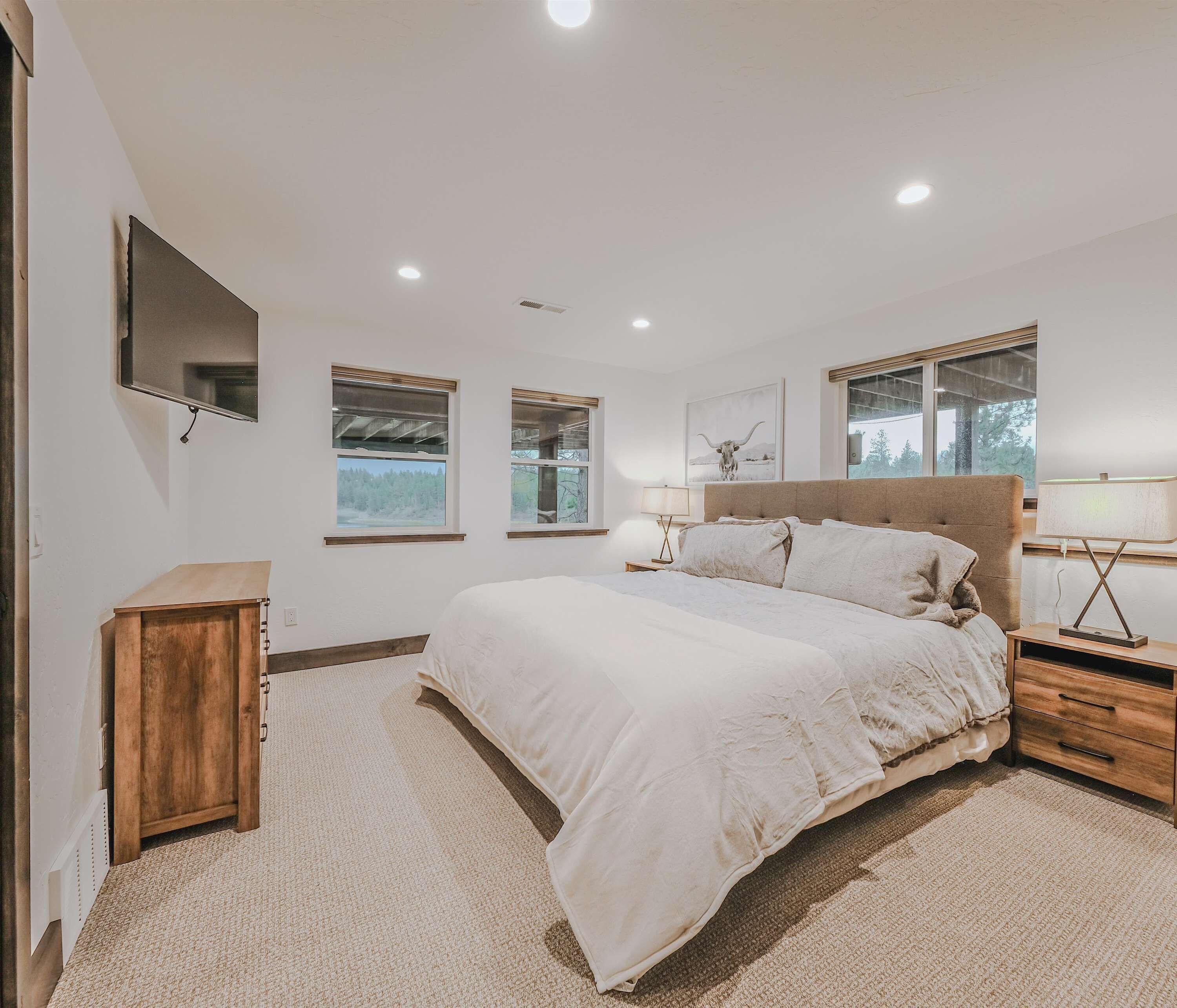 A bedroom with a large bed, a wooden nightstand, a bedside lamp, and a mounted TV.