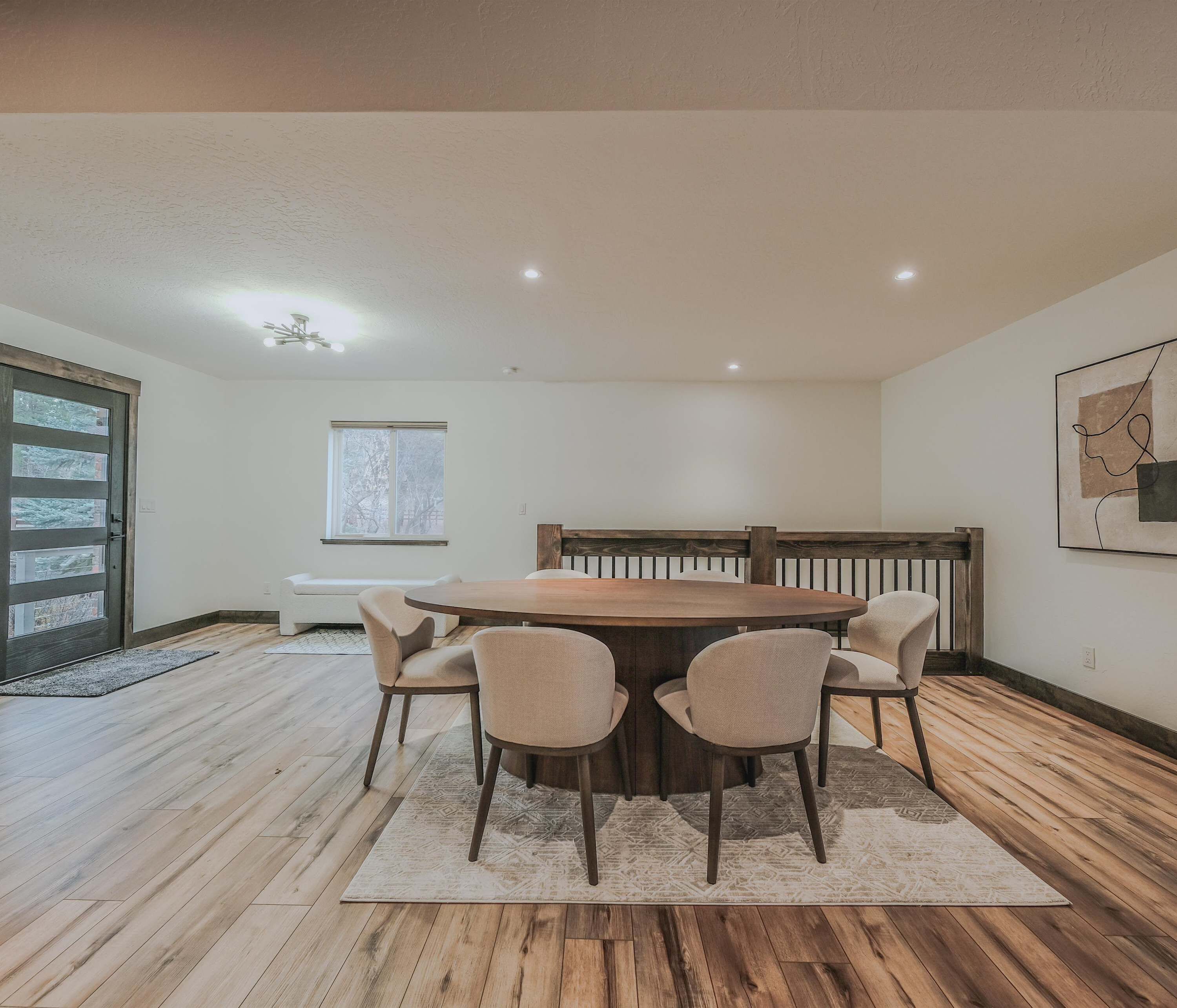 A dining area with a wooden table and four chairs, a white radiator, a window with a view of trees, and a door with glass panels.