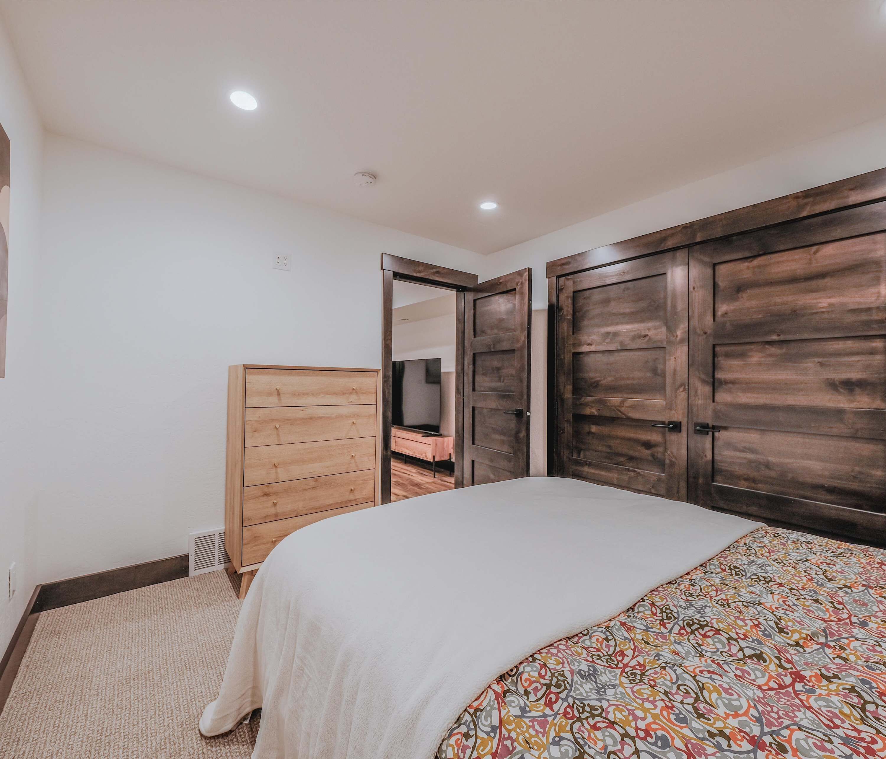 A bedroom with a bed, wooden wardrobe, and a mirror.