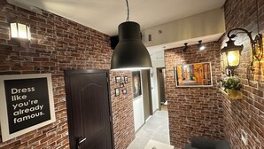 A hallway with brick walls, a black door, a white table with a plant, and a framed picture with text. - Luxury Hostel Bedspace in Downtown (Dubai)