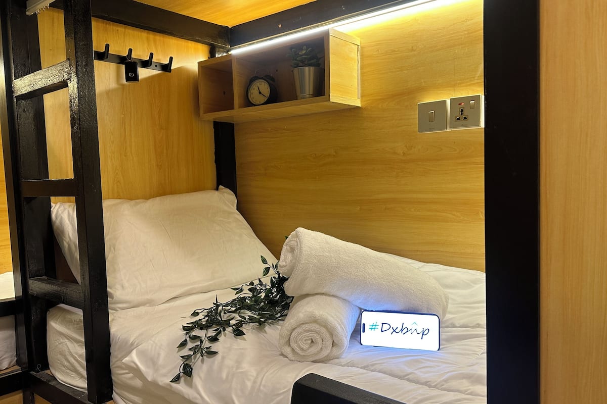 A cozy room with a wooden bed, a small shelf with a clock and a plant, and a sign with a hashtag.