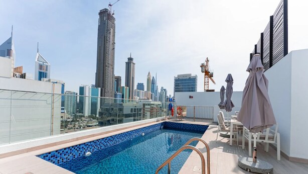 A rooftop pool with a city skyline view, a glass railing, and a seating area with umbrellas. - Luxury Hostel Bedspace in Downtown (Dubai)