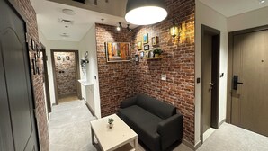 A modern living room with a brick wall, a black sofa, a small table, and a hanging light fixture. - Luxury Hostel Bedspace in Downtown (Dubai)