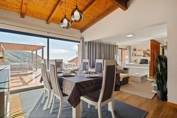 A dining area with a table set for six, large windows, and a view of the outdoors.