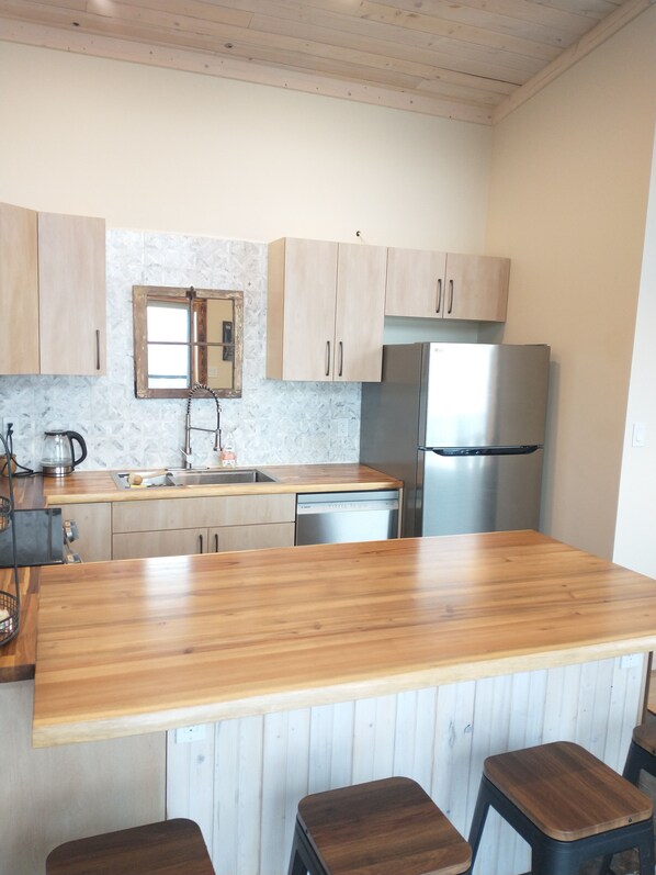 A kitchen with wooden cabinets, a stainless steel refrigerator, a sink, and a wooden countertop.