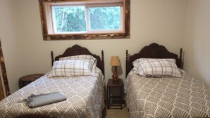 Une chambre avec deux lits en bois, dotés de têtes de lit assorties, une petite table de chevet avec une lampe et une fenêtre située au-dessus des lits.