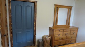 Une pièce avec une porte bleue, une commode en bois dotée de tiroirs, un miroir et un panier en osier.