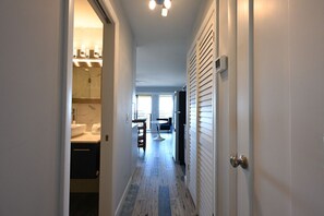 A hallway with a bathroom on the left, a dining area with a table and chairs in the center, and a bedroom with a window on the right. - Blue Heaven Oceanfront Condo in Hilton Head (Hilton Head Island)