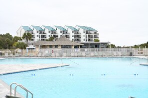 A swimming pool with lounge chairs, a building with balconies, and a lifeguard tower. - Blue Heaven Oceanfront Condo in Hilton Head (Hilton Head Island)
