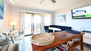 Ein Wohnzimmer mit einer Couch, einem Couchtisch, einem Fernseher und einem Balkon.