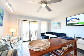 A living room with a sofa, a coffee table, a TV, and a balcony. - Blue Heaven Oceanfront Condo in Hilton Head (Hilton Head Island)