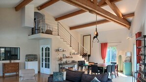 Un vaste espace de vie doté d’un haut plafond, de poutres apparentes, d’un escalier, d’un coin repas et d’une cuisine.
