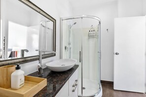 A modern bathroom with a glass-enclosed shower, a white sink, and a large mirror.