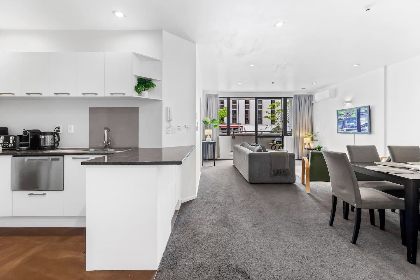 A modern kitchen with white cabinetry, a built-in dishwasher, and a coffee station.