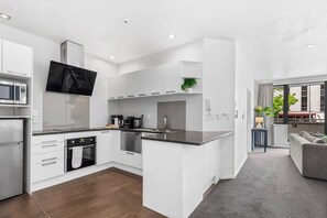 A modern kitchen with white cabinetry, a flat-screen TV, and a dining area with a grey sofa. - City Centre Living Meets Comfort by Zodiak (Auckland)