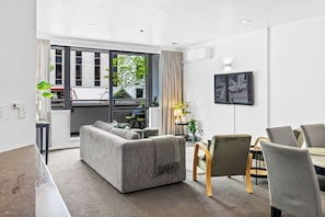 A modern living room with a sofa, dining table, chairs, and a TV. - City Centre Living Meets Comfort by Zodiak (Auckland)