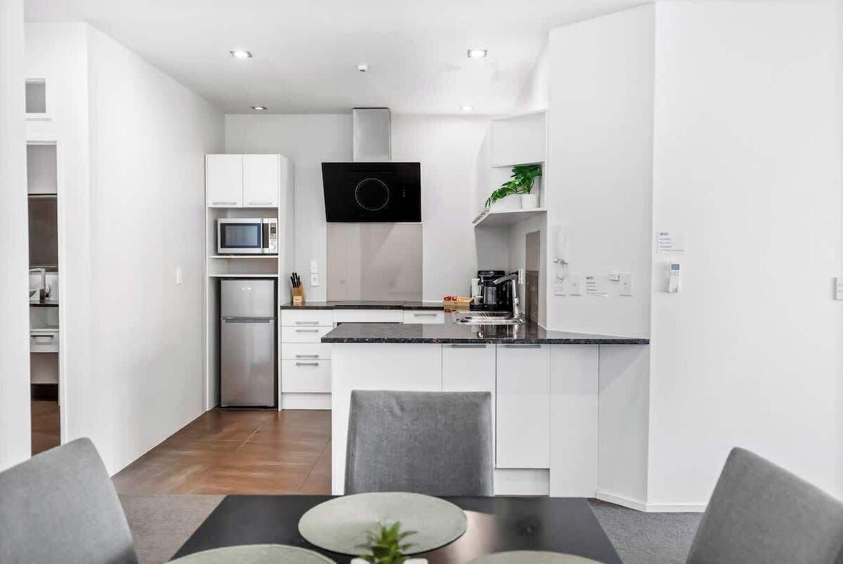 A modern kitchen with white cabinetry, a built-in microwave, and a black range hood.