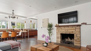 Ein modernes Wohnzimmer mit Kamin, einem Essbereich mit Barhocker und einer Küche mit großem Fenster.