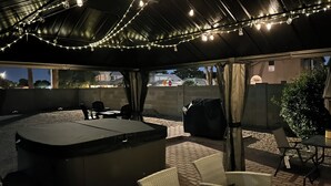 Un patio exterior con zona de estar techada, luces colgantes y un jacuzzi.