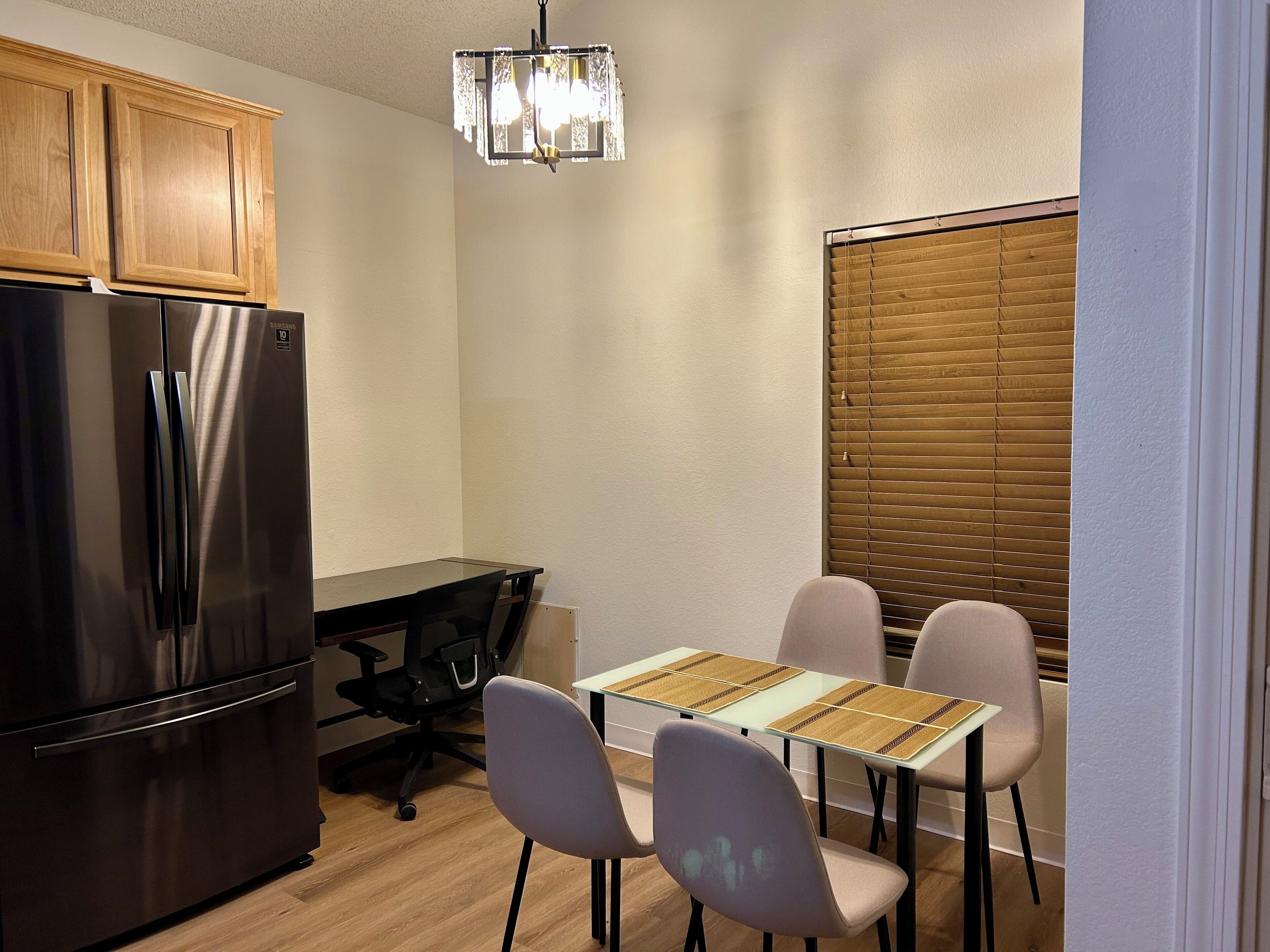 Une cuisine compacte équipée d’un réfrigérateur, d’une table à manger avec quatre chaises et d’un lustre.