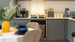 Eine moderne Küche mit grauen Schränken, einer weißen Arbeitsplatte und einem Essbereich mit Tisch für zwei Personen.