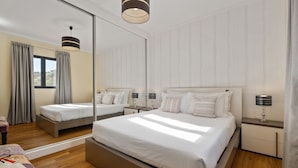 Ein modernes Hotelzimmer mit einem großen Bett, Nachttischen, einem Spiegel und Blick ins Freie.