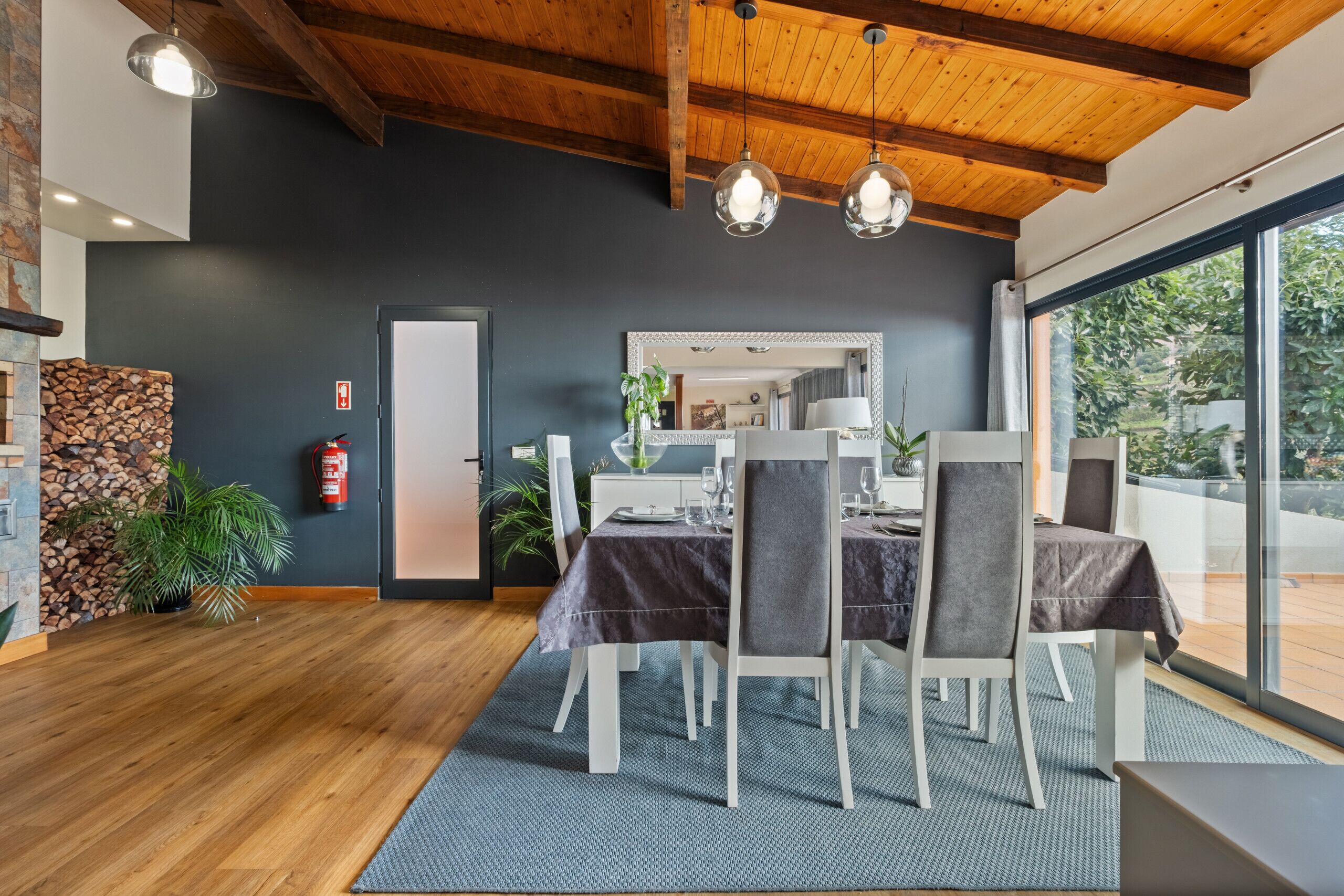 Un espace de restauration moderne avec un plafond en bois, un mur en pierre et une grande fenêtre donnant sur un paysage verdoyant.