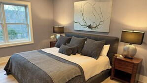 Un dormitorio con una cama grande, dos mesitas de noche, un ventanal y una obra de arte en la pared.